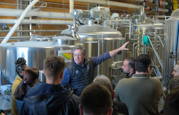 A group of people listening to a man speak inside a warehouse.